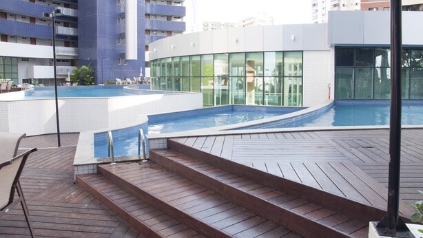 A rooftop swimming pool with steps leading to it, surrounded by a wooden deck and lounge chairs. - Beach Class Residence by SOLEMAR (Fortaleza)
