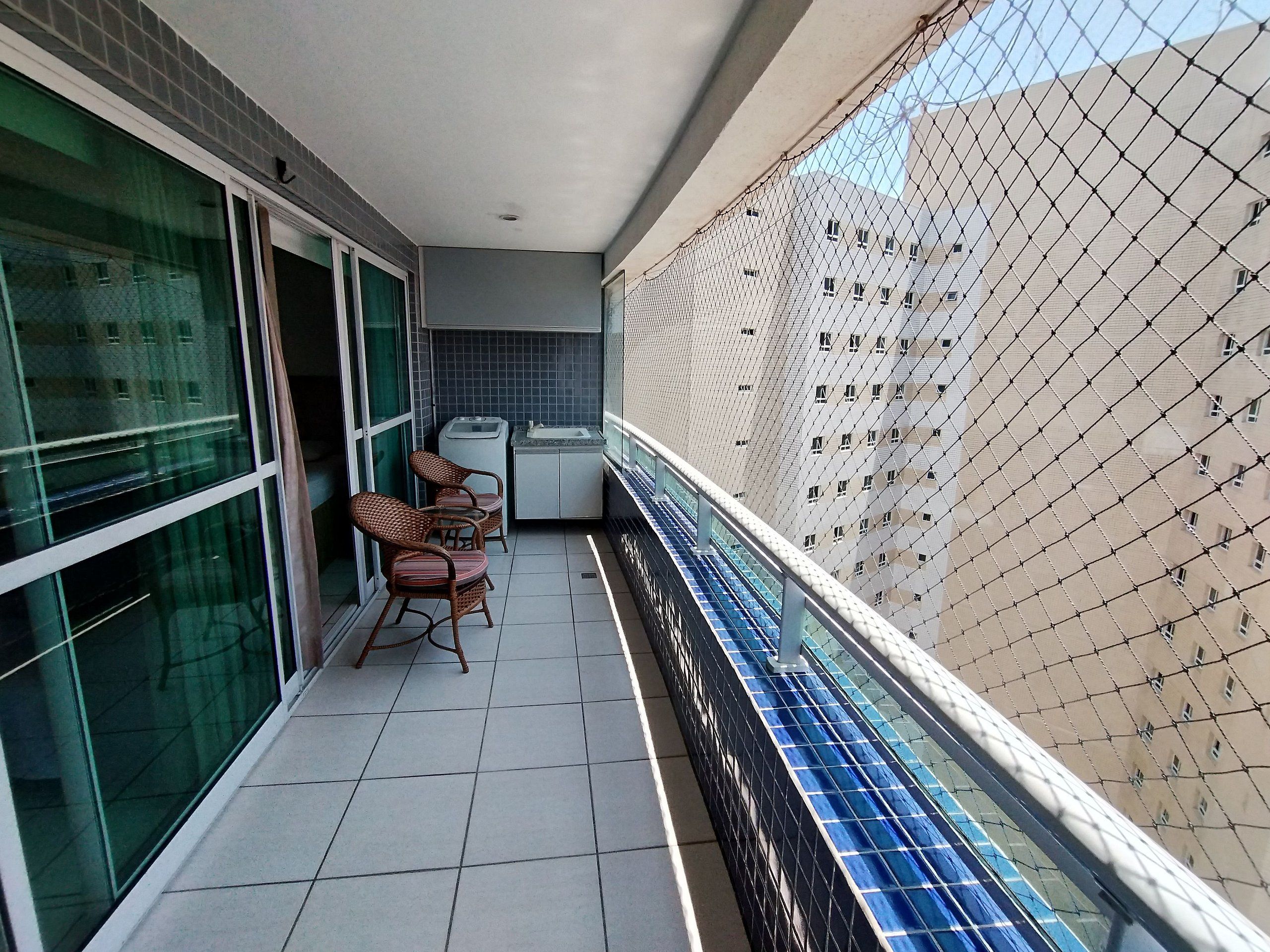 Ein Balkon mit Fliesenboden, einer kleinen Küchenzeile und zwei Korbstühlen.