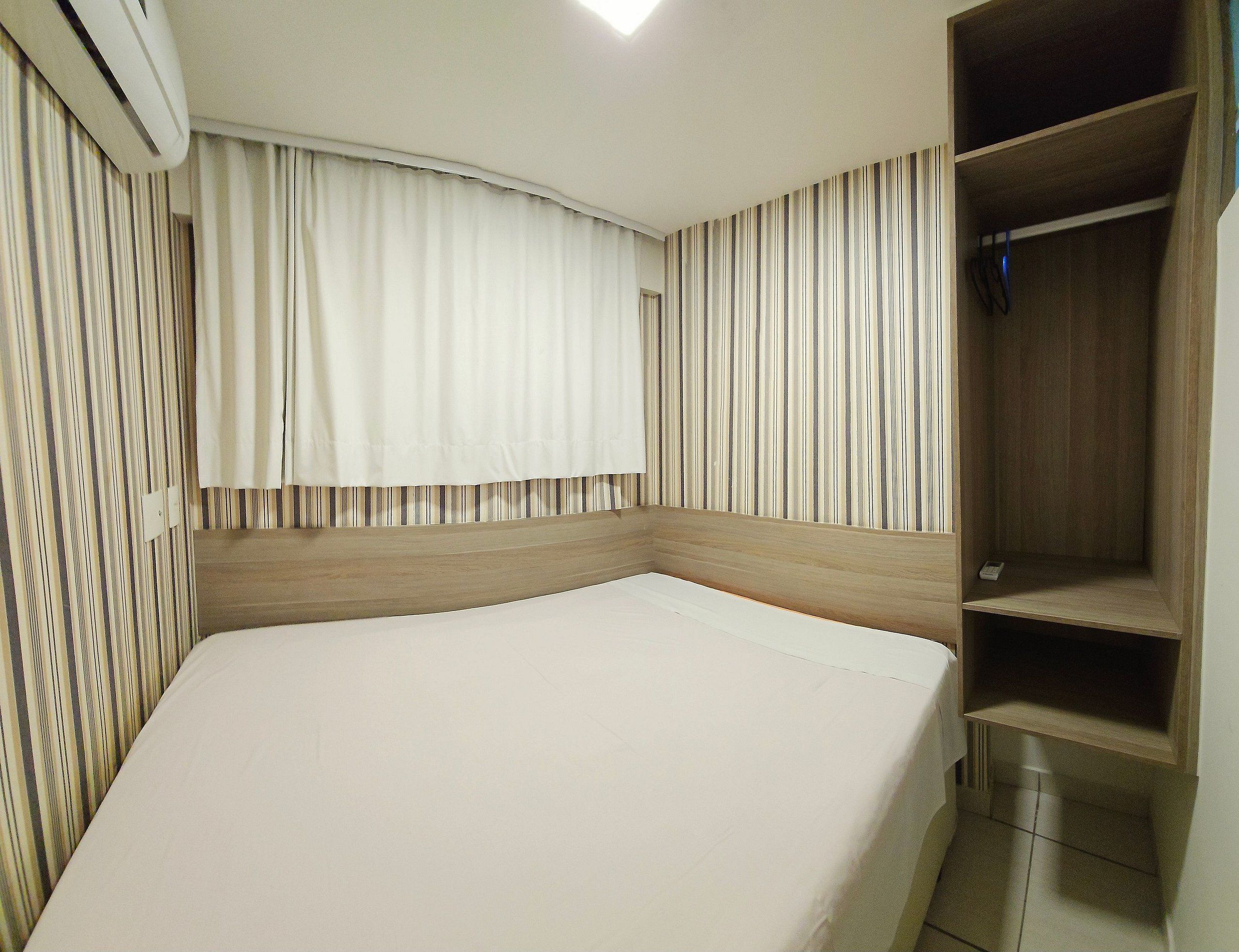 A hotel room with a bed, a wooden headboard, a wardrobe, and a striped curtain.