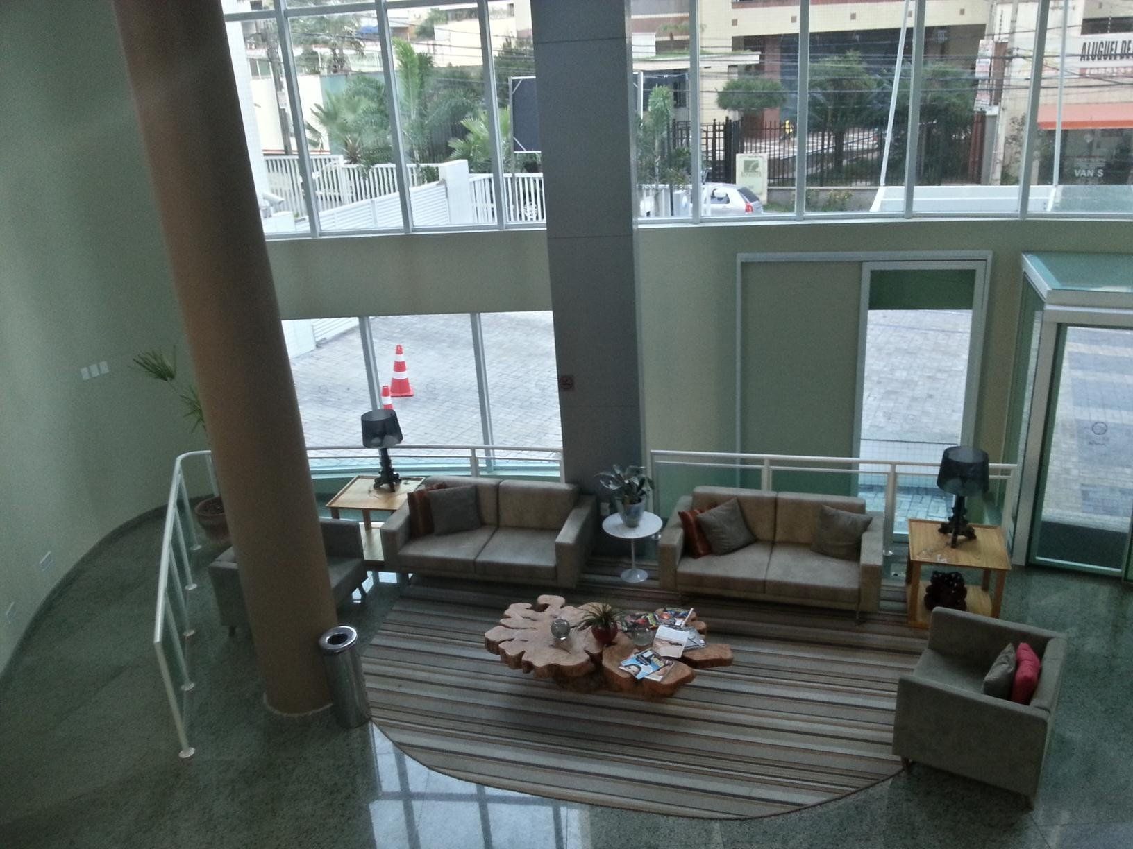 A spacious lobby with a high ceiling, a central seating area with sofas and a coffee table, and large windows offering a view of the street outside.
