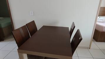 Een rechthoekige eettafel met vier stoelen, een vloer van witte tegels en een effen witte muur.