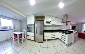 Une cuisine moderne avec des meubles blancs, un réfrigérateur en acier inoxydable, un four à micro-ondes et une cuisinière à gaz. On y trouve une table à manger avec des chaises rouges et une fenêtre avec des rideaux.