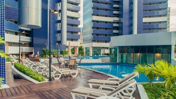 A pool area with lounge chairs, a wooden deck, and a modern building with balconies. - Beach Class Residence by SOLEMAR (Fortaleza)
