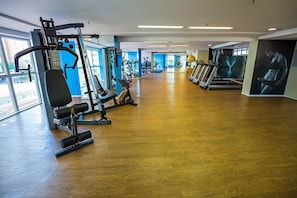 Un gimnasio con máquinas de cardio, equipo de levantamiento de pesas y suelo de madera.