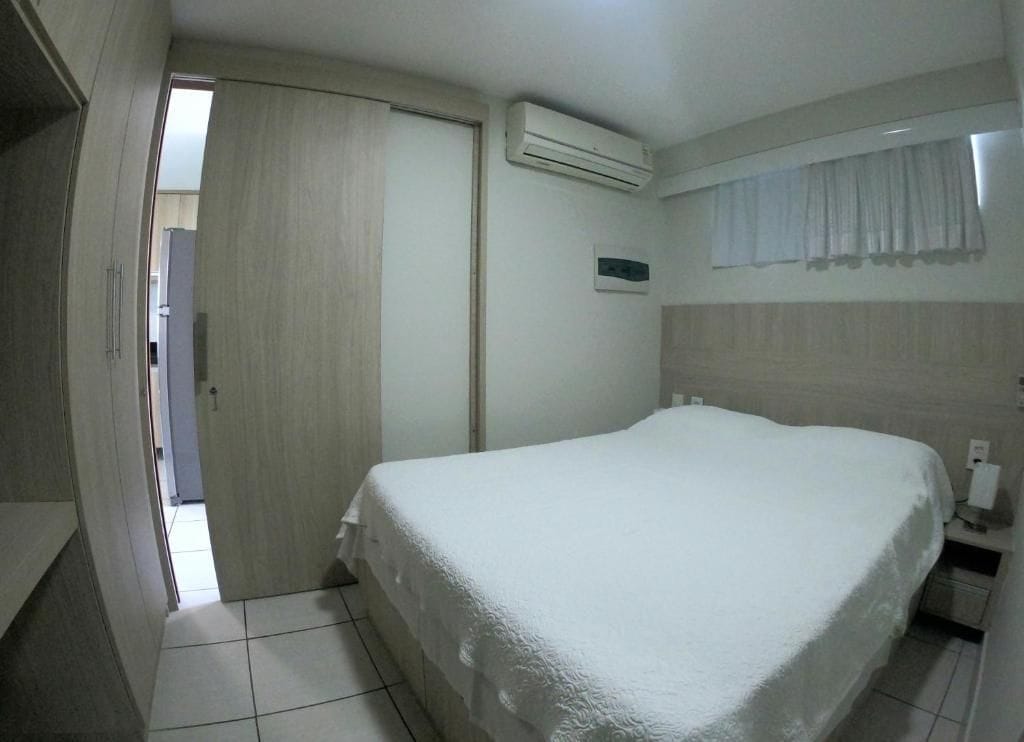 A bedroom with a bed, an air conditioning unit, a window with curtains, and a door leading to another room.