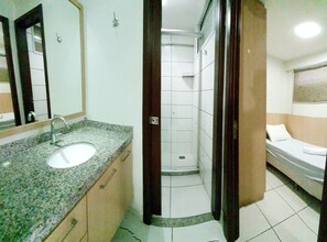 Ein Badezimmer mit Waschbecken, Spiegel, Dusche und einem Bett.