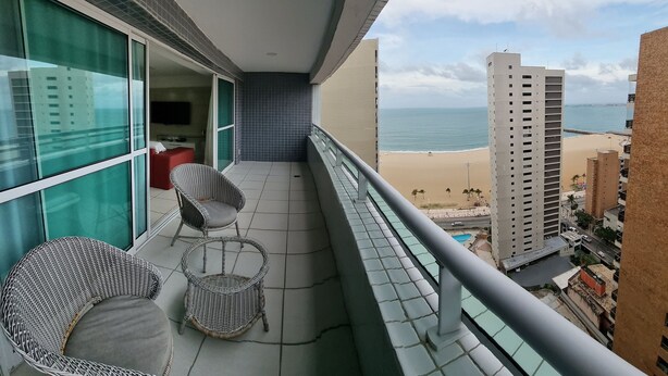 A balcony with two wicker chairs, a small table, and a view of the beach and ocean. - Beach Class Residence by SOLEMAR (Fortaleza)