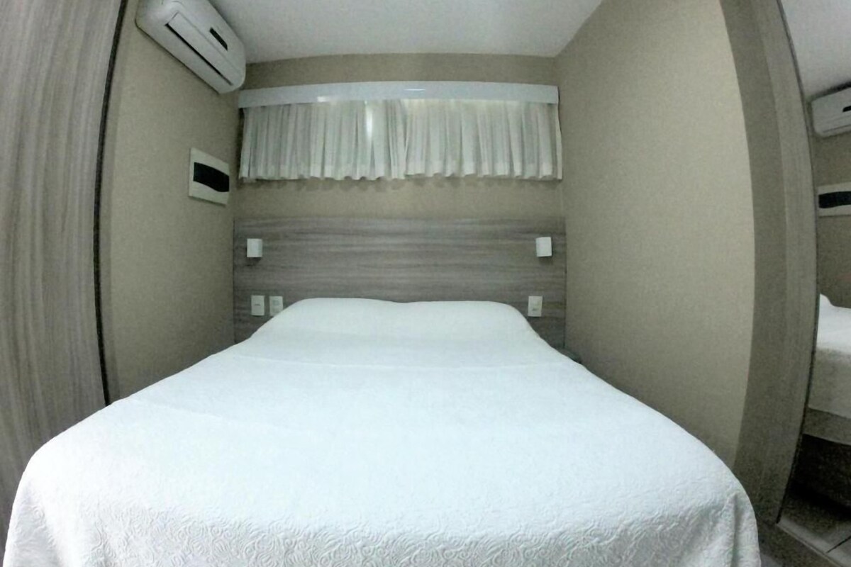 A hotel room with a bed, air conditioning unit, curtains, and a headboard.