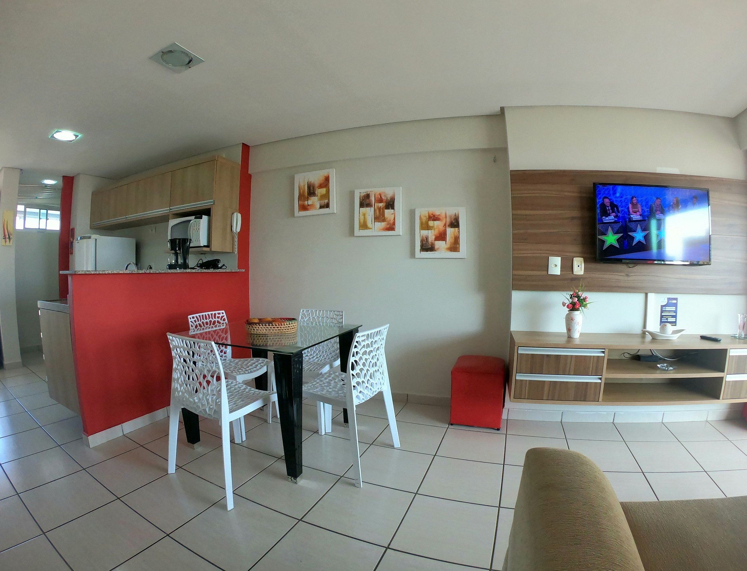 A modern living room with a dining area, a kitchen, and a TV mounted on the wall.
