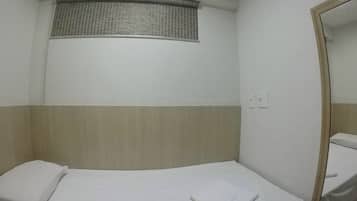 A small, single-bed room with a window, a mirror, and a wall-mounted air conditioning unit.