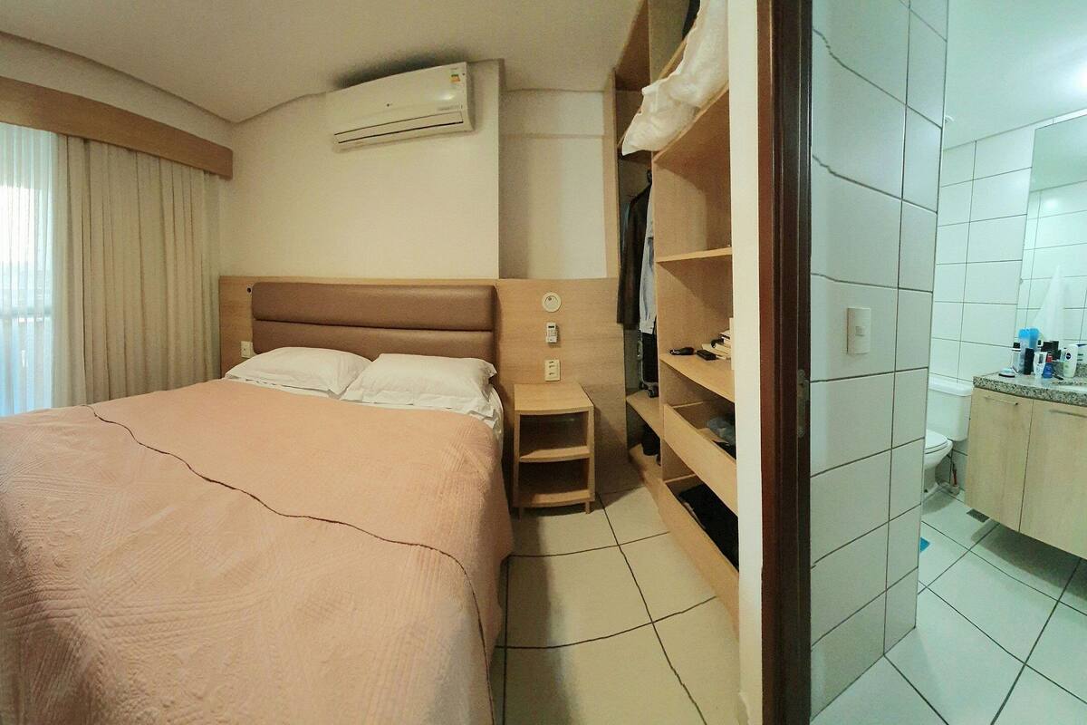 Et hotelværelse med seng, natbord, garderobeskab og aircondition samt badeværelse.