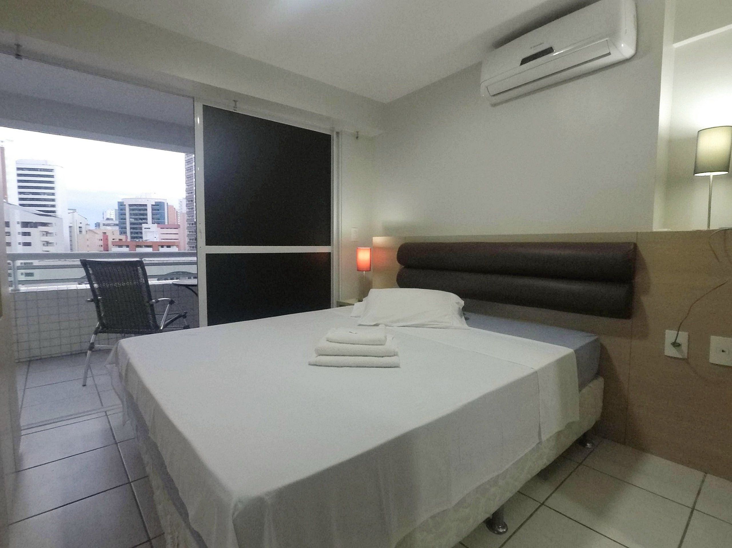 Una habitación de hotel con una cama, una ventana, una silla y un equipo de aire acondicionado.