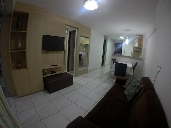 Una sala de estar con televisor, sofá, mesa de centro y un comedor con sillas y mesa.