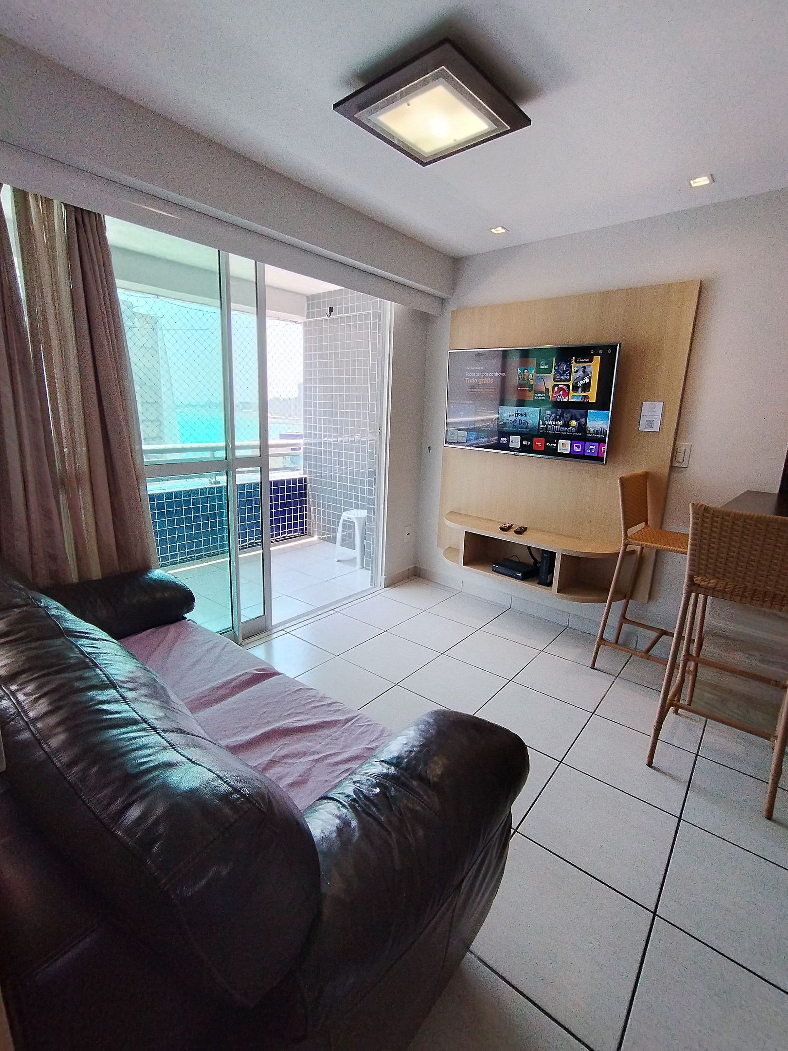 Un salon avec un canapé en cuir, un téléviseur fixé au mur et un balcon offrant une vue dégagée.