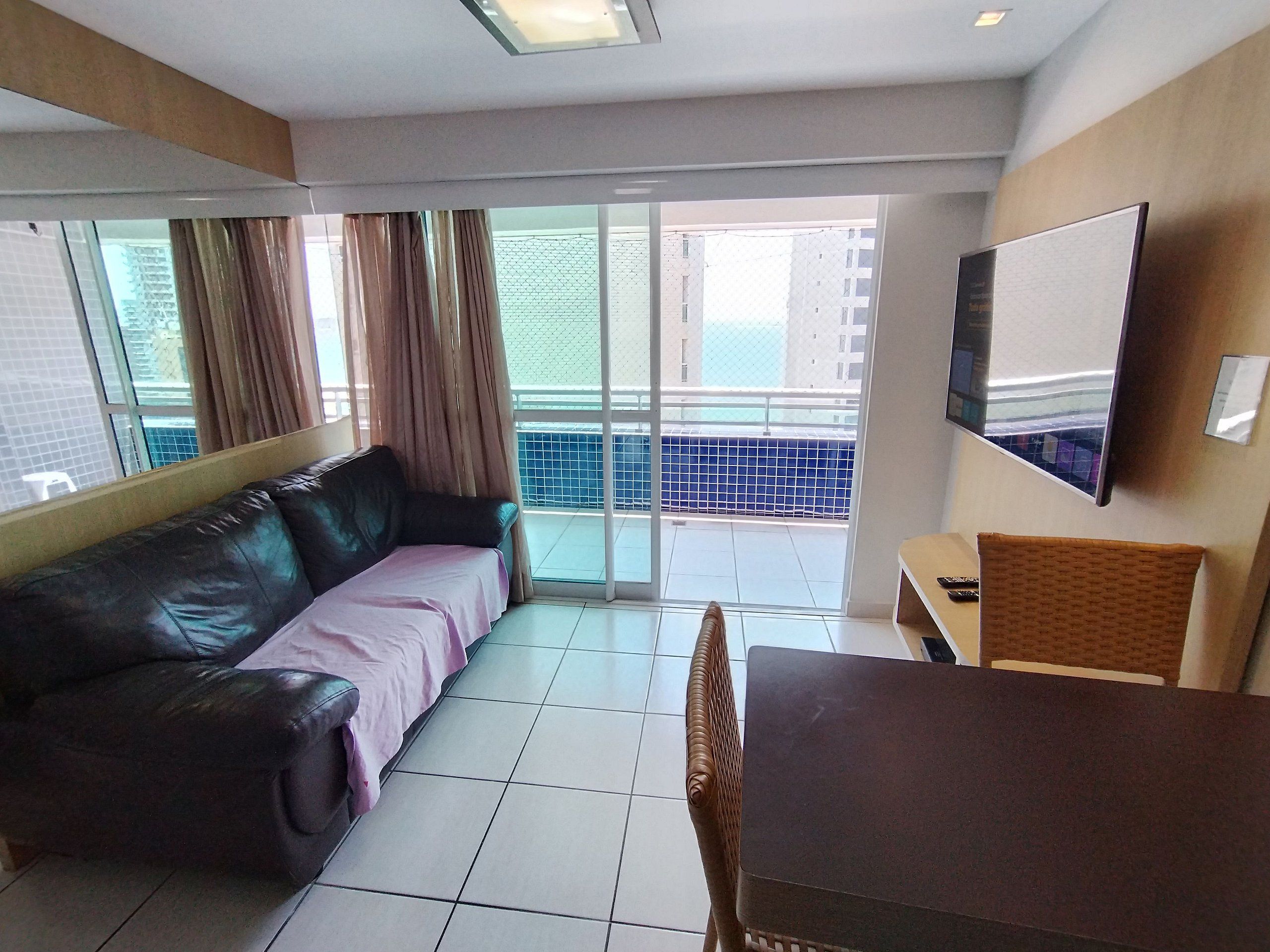 Una habitación con sofá, mesa, televisor y balcón con vistas.