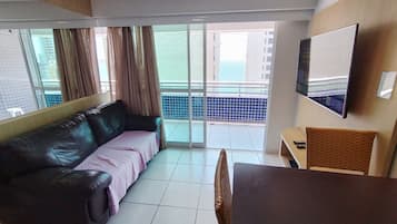 A room with a sofa, a table, a TV, and a balcony with a view.