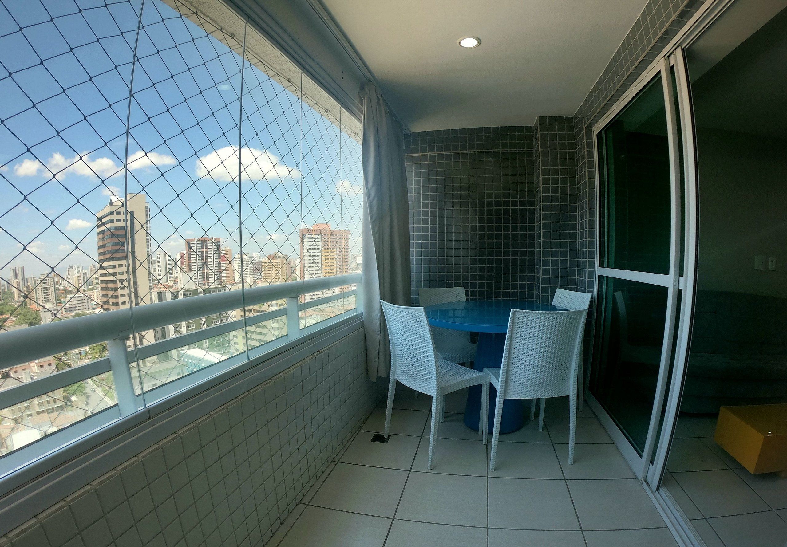 Un balcón con vistas a edificios de la ciudad, una mesa azul y sillas blancas.