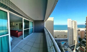 Un balcon avec vue sur la plage et l’océan, un sol carrelé et une chaise rouge.