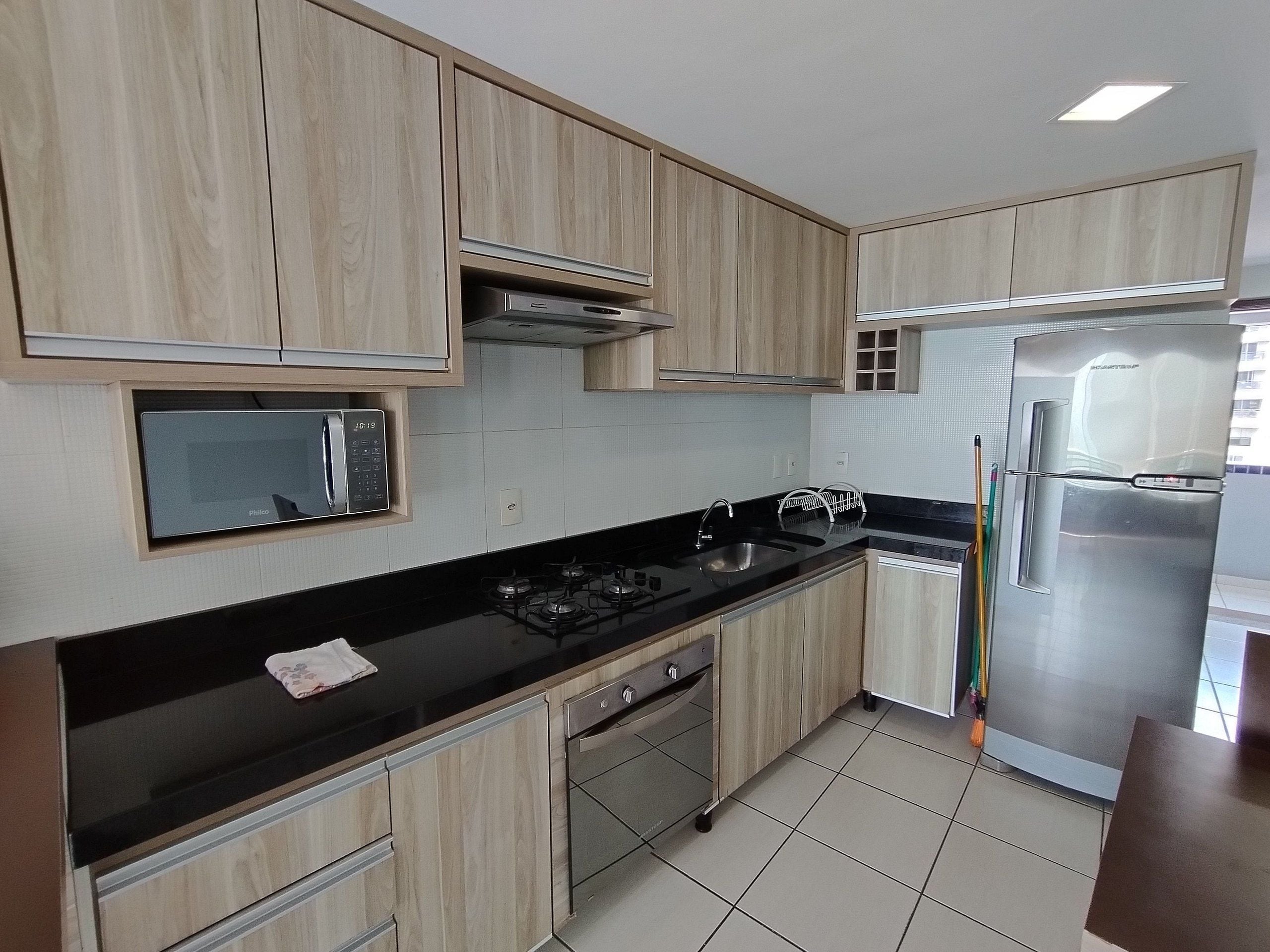Una cocina moderna con gabinetes de madera, microondas integrado, estufa a gas, refrigerador de acero inoxidable y lavavajillas.