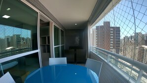 A balcony with a blue table and chairs, a glass partition, and a view of city buildings. - Beach Class Residence by SOLEMAR (Fortaleza)