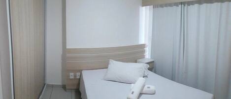 Habitación de hotel con cama, almohada, control remoto, unidad de aire acondicionado y ventana con cortinas.