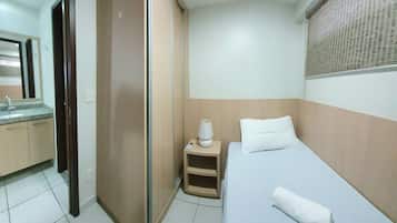 Quarto de hotel com cama, mesa de cabeceira com abajur, espelho, banheiro com pia e janela com persianas.