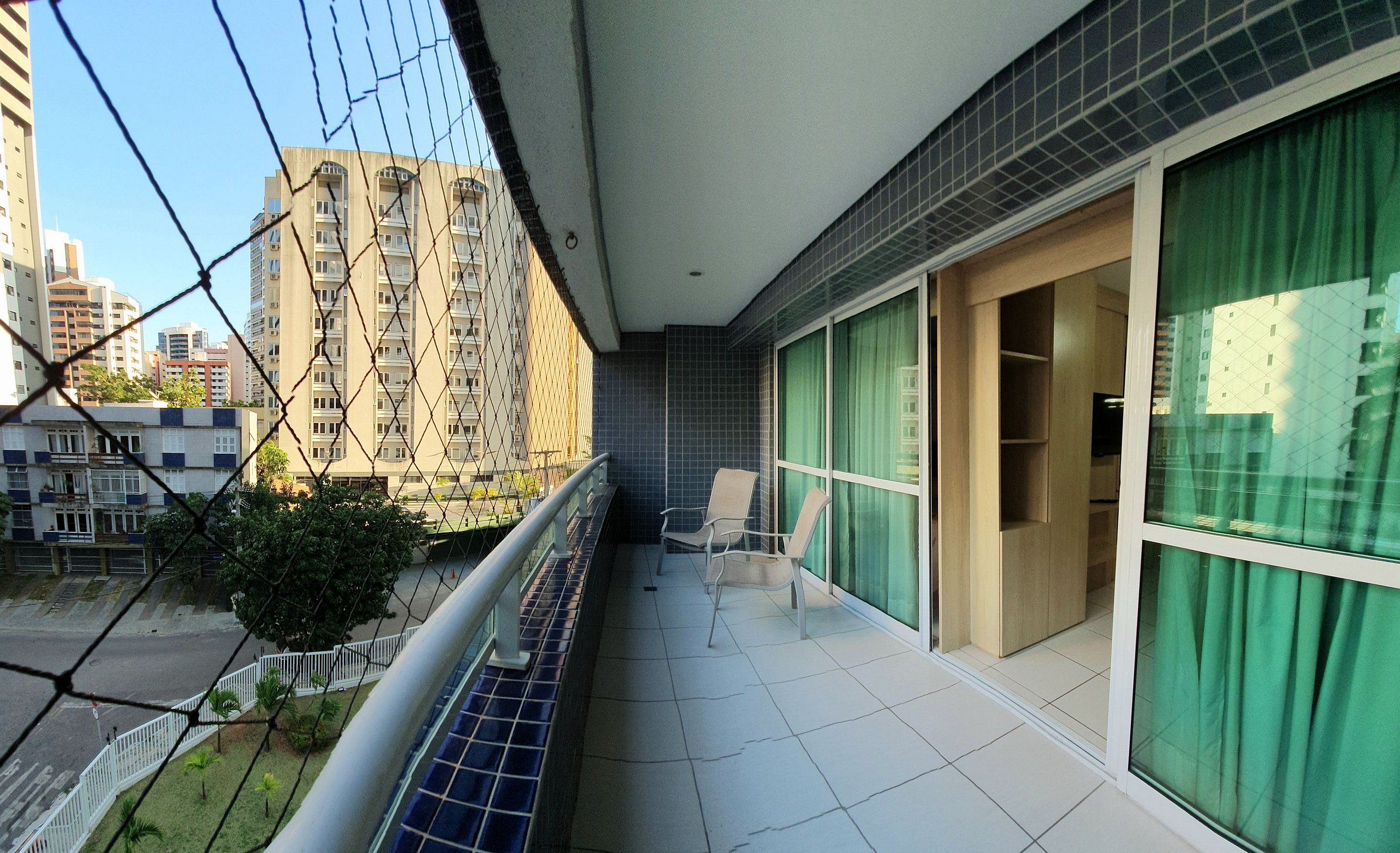 A balcony with a view of tall residential buildings, a metal railing, and a door leading to a room with a green curtain.