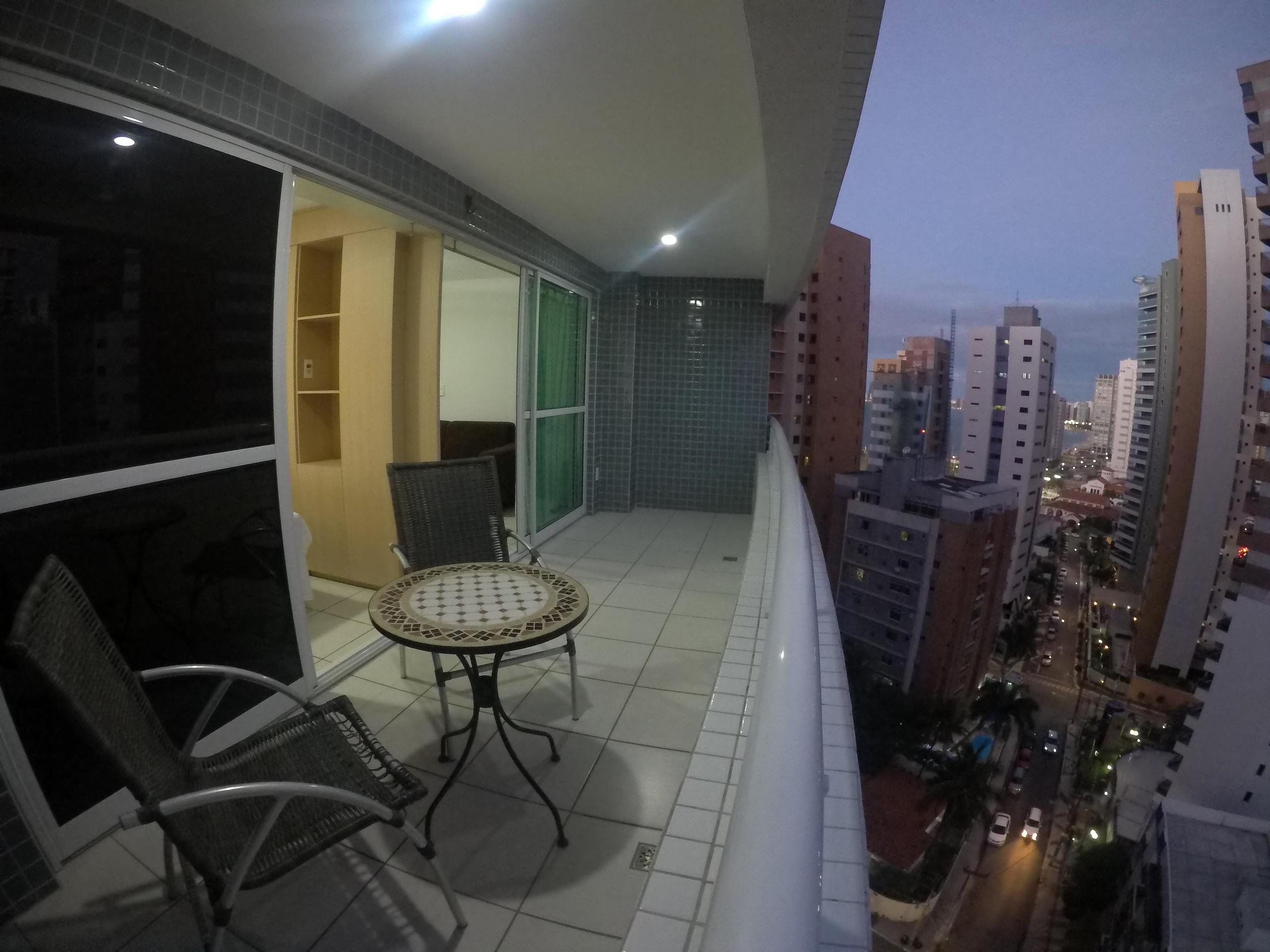 A balcony with a table and chairs, a sliding glass door, and a cityscape view.
