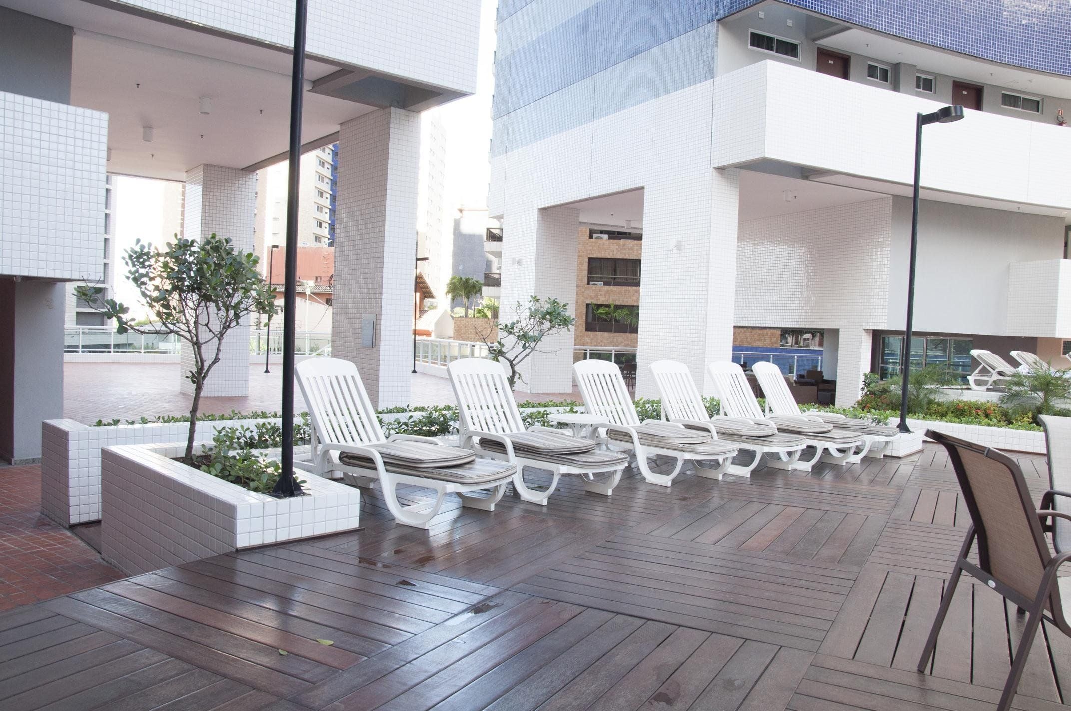 Un área de descanso en la azotea con sillones blancos, una terraza de madera y vistas de los edificios circundantes.