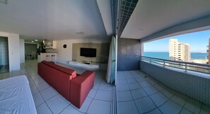 A modern living room with a red sofa, a flat-screen TV, and a balcony with a city view. - Beach Class Residence by SOLEMAR (Fortaleza)