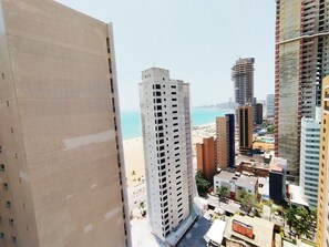 Ein Hochhaus mit einer rasterartigen Fassade, Blick auf einen Strand und weitere umliegende Gebäude.