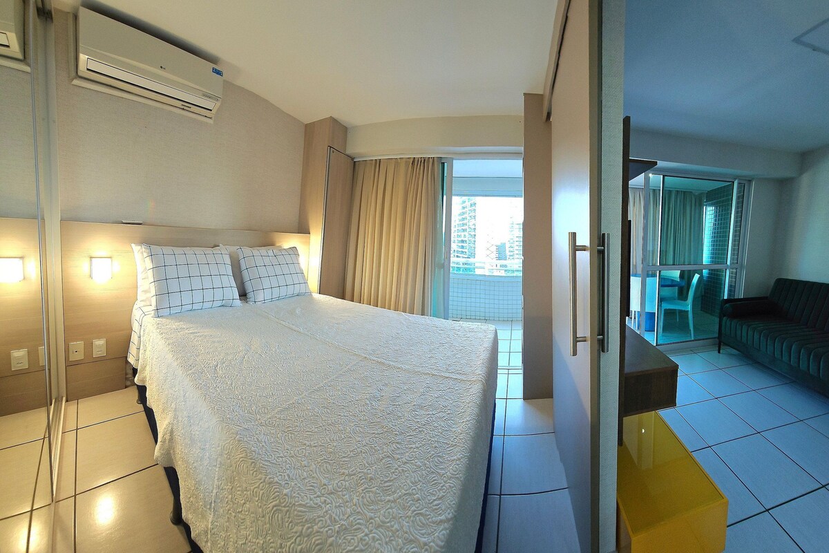 A hotel room with a bed, a sliding door to a balcony, a sofa, and a small table.