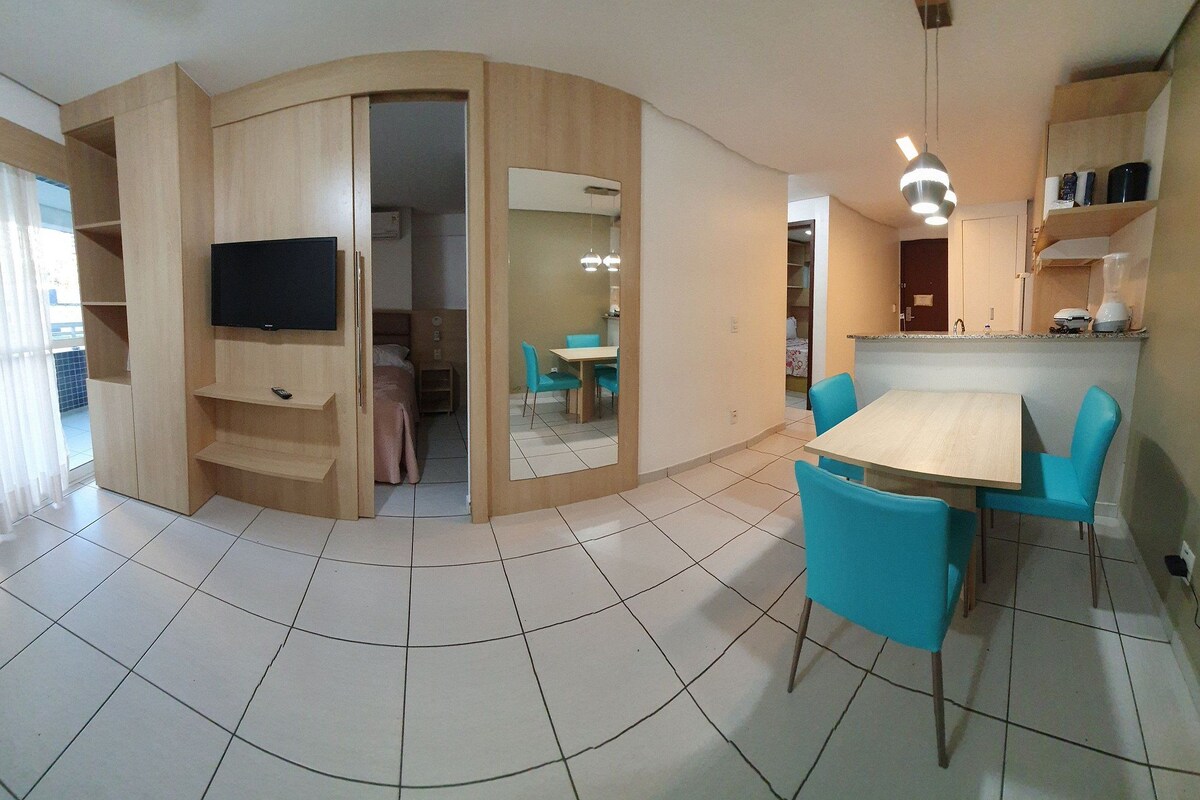 A compact living space with a TV, dining table, chairs, and a kitchenette.