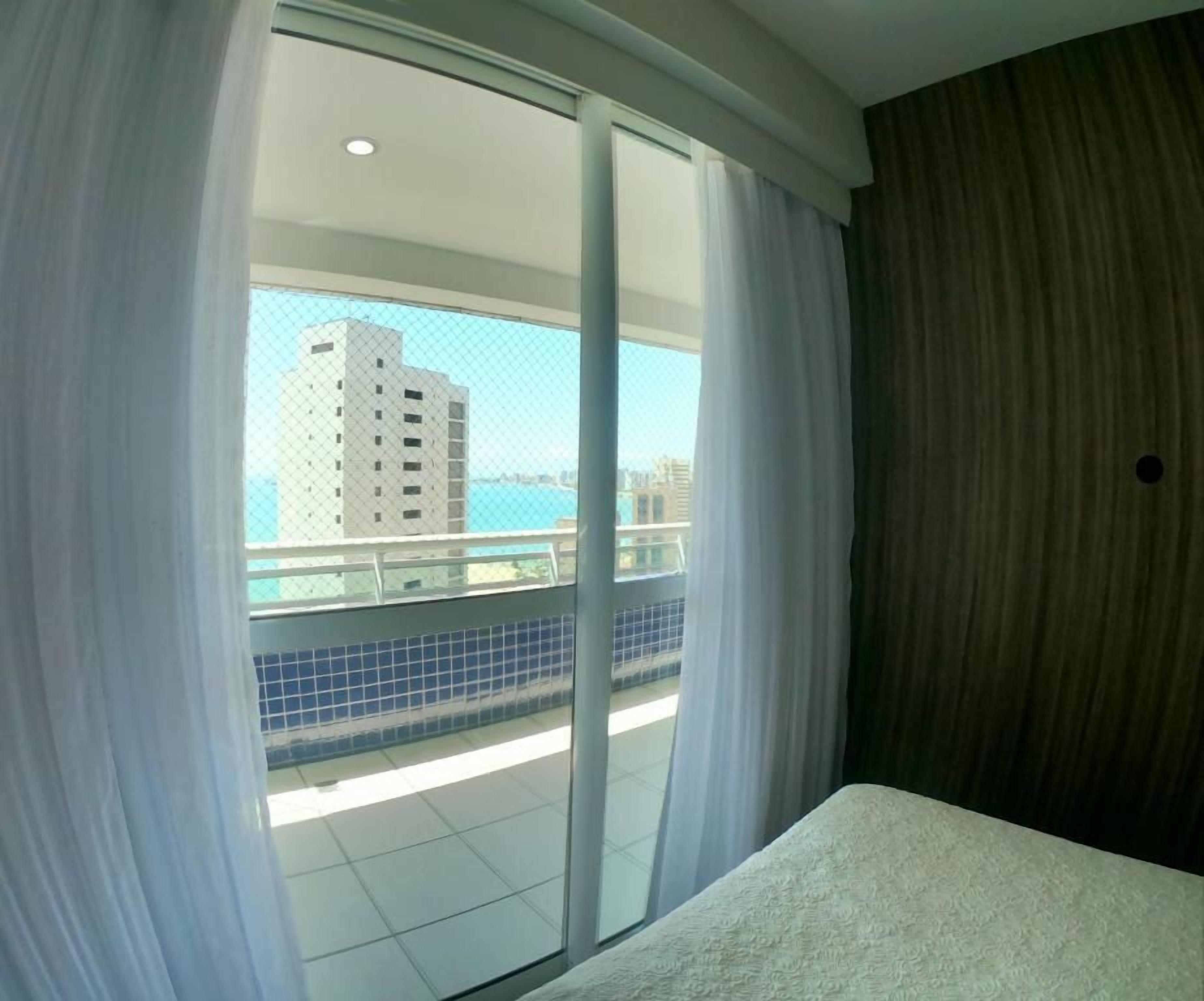 A hotel room with a balcony, a view of a building, and a tiled floor.