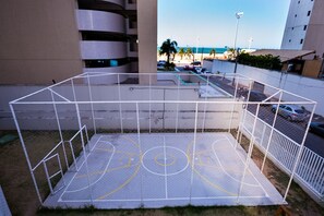 A basketball court enclosed by a white fence, with a view of a beach and a parking area in the background. - Beach Class Residence by SOLEMAR (Fortaleza)