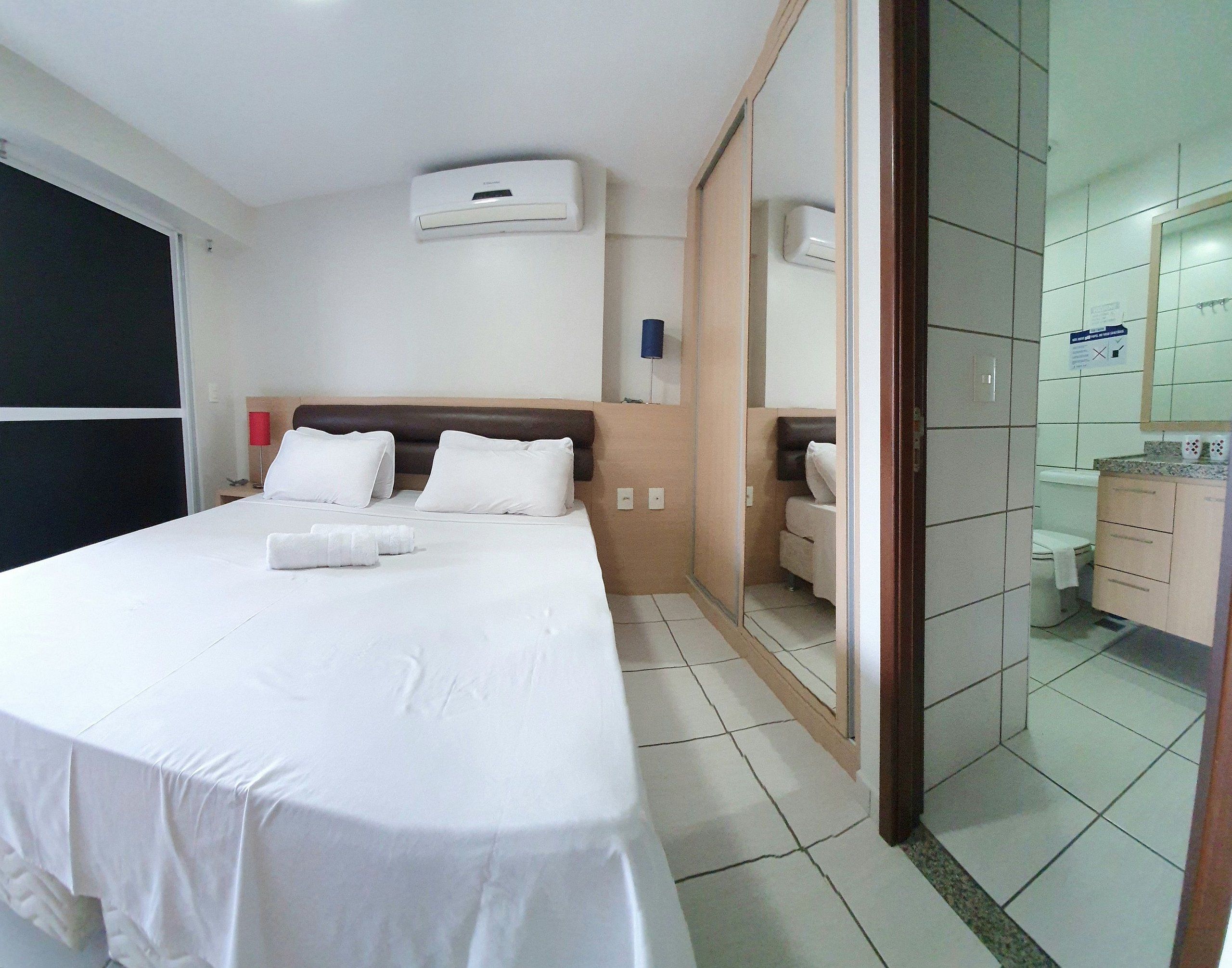 Habitación de hotel con cama, mesita de noche, espejo y baño visible a través de una puerta abierta.