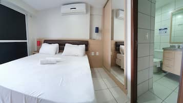 Habitación de hotel con cama, mesita de noche, espejo y baño visible a través de una puerta abierta.