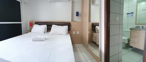 A hotel room with a bed, a bedside table, a mirror, and a bathroom visible through an open door.