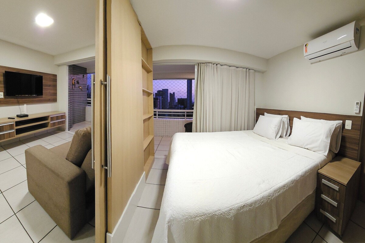 Ein Hotelzimmer mit Bett, Fernseher, einer Couch und einem Balkon mit Blick auf die Stadt.