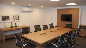 Uma sala de conferências com uma mesa comprida, cadeiras pretas, uma TV na parede e obras de arte.