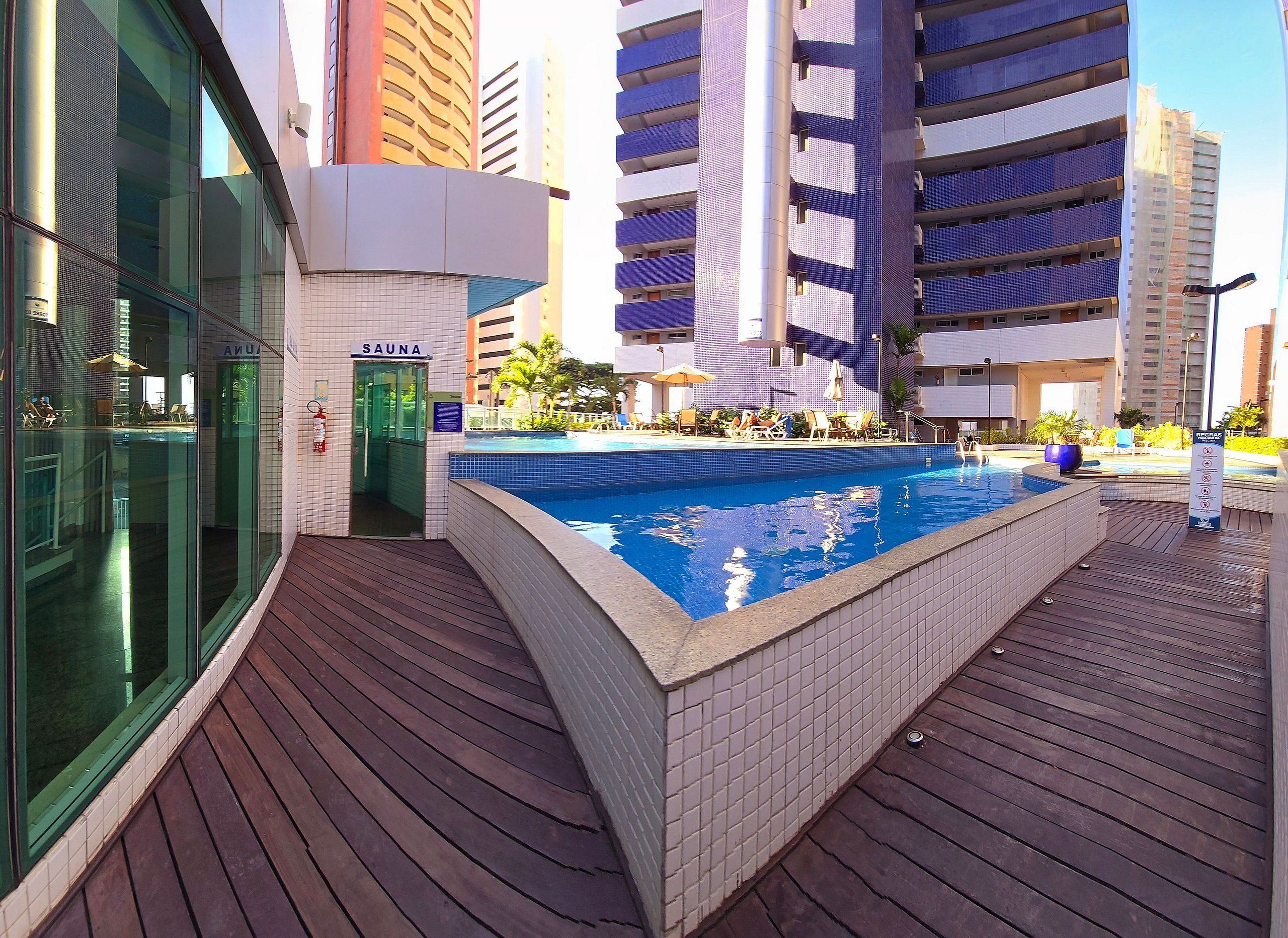 Una piscina con plataforma de baldosas, sauna y entrada por puerta de vidrio.