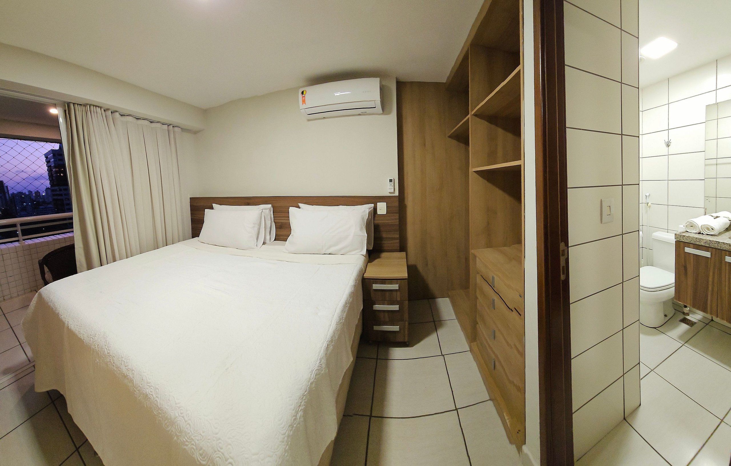 Une chambre d’hôtel comprenant un lit, une armoire en bois, une salle de bain avec des toilettes et un appareil de climatisation.