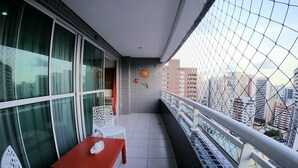A balcony with a table and chairs, a view of the cityscape, and a tiled wall. - Beach Class Residence by SOLEMAR (Fortaleza)