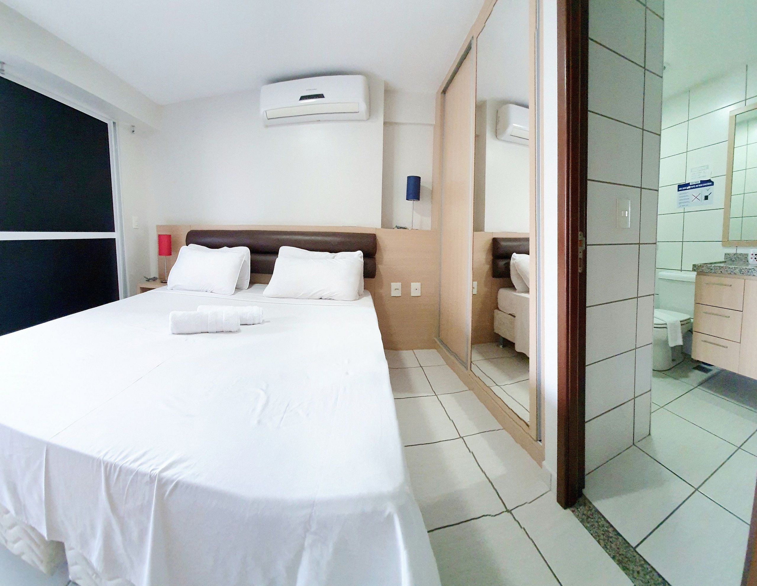 Une chambre d’hôtel avec un lit, une table de chevet et une salle de bain visible à travers une porte ouverte.