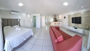 A modern hotel room with a bed, a red sofa, a TV, and a kitchenette. - Beach Class Residence by SOLEMAR (Fortaleza)