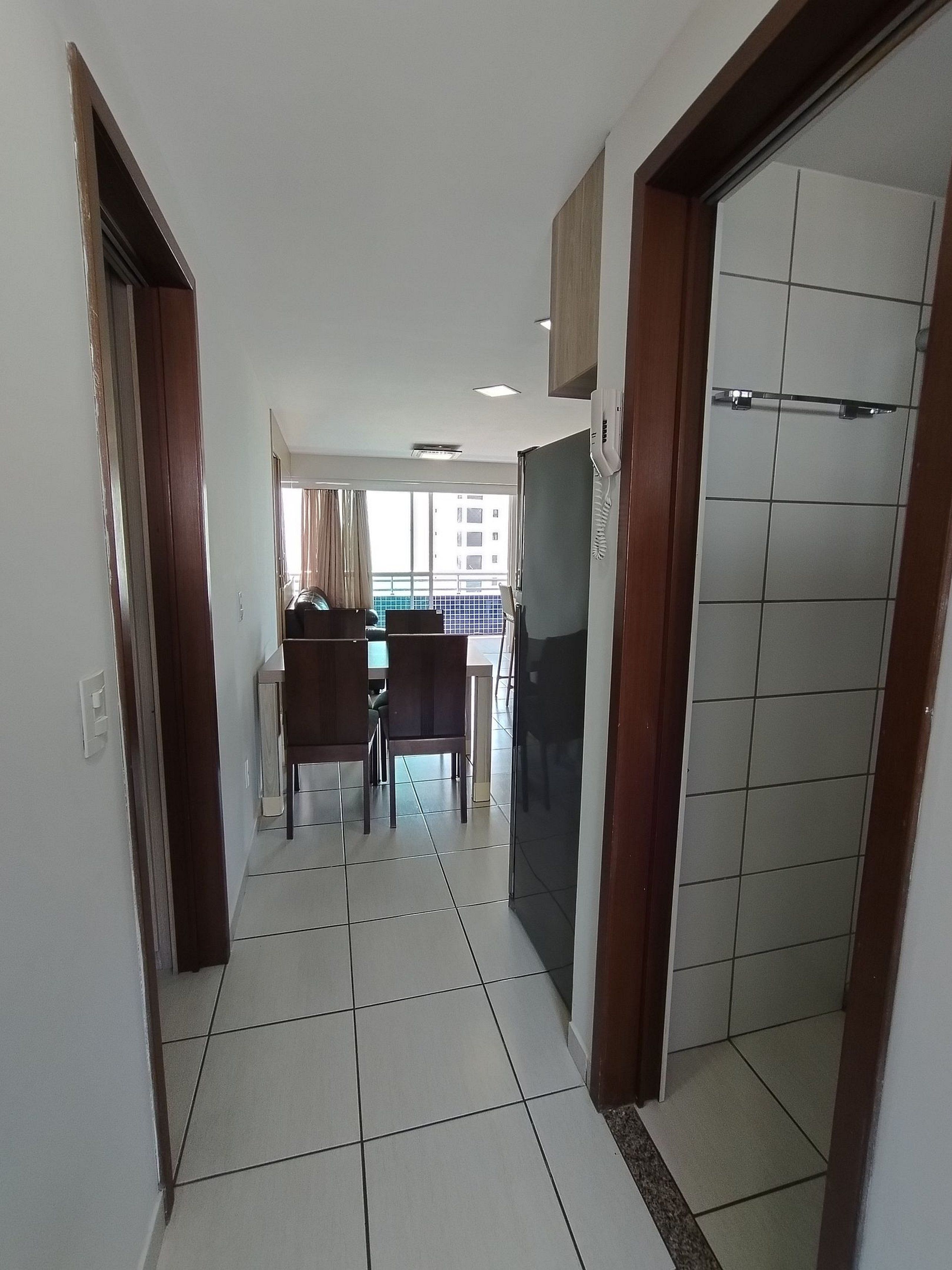 A hallway with a dining area, a view of a building, and a tiled floor.