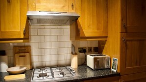 A kitchen with wooden cabinets, a gas stove, a toaster, and a brick backsplash. - Newly Refurbed Home With Free Parking (Edinburgh)