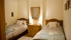 A bedroom with two single beds, a nightstand between them, a mirror above the nightstand, and a small wall-mounted shelf. - Newly Refurbed Home With Free Parking (Edinburgh)