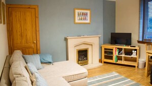 A living room with a beige sofa, a fireplace, a television, and a bookshelf. - Newly Refurbed Home With Free Parking (Edinburgh)