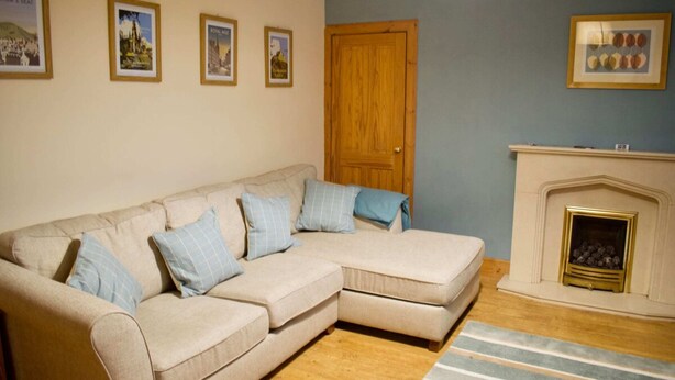 A living room with a beige sectional sofa, a wooden door, and a fireplace. - Newly Refurbed Home With Free Parking (Edinburgh)